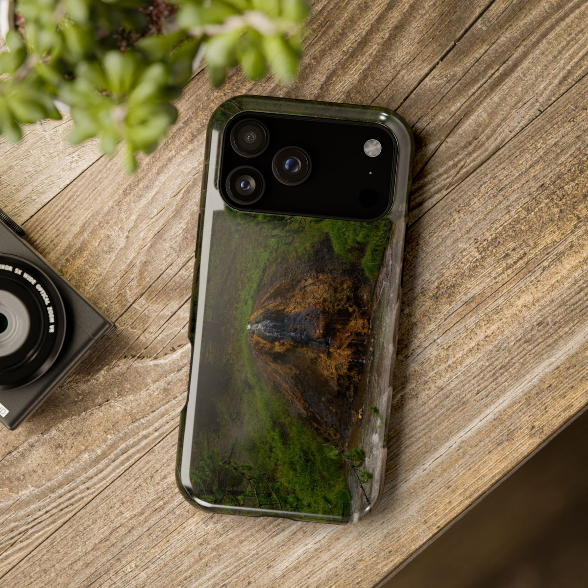 Lifestyle mockup of Chocolate Pot Hot Spring phone case standing on a wood surface with natural decor, featuring original Yellowstone photography by My Blu Horizon.